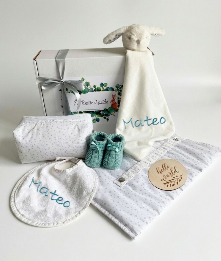 Canastilla de regalo para bebé con doudou de conejo, babero personalizado, patucos de punto verde y neceser de estrellas.