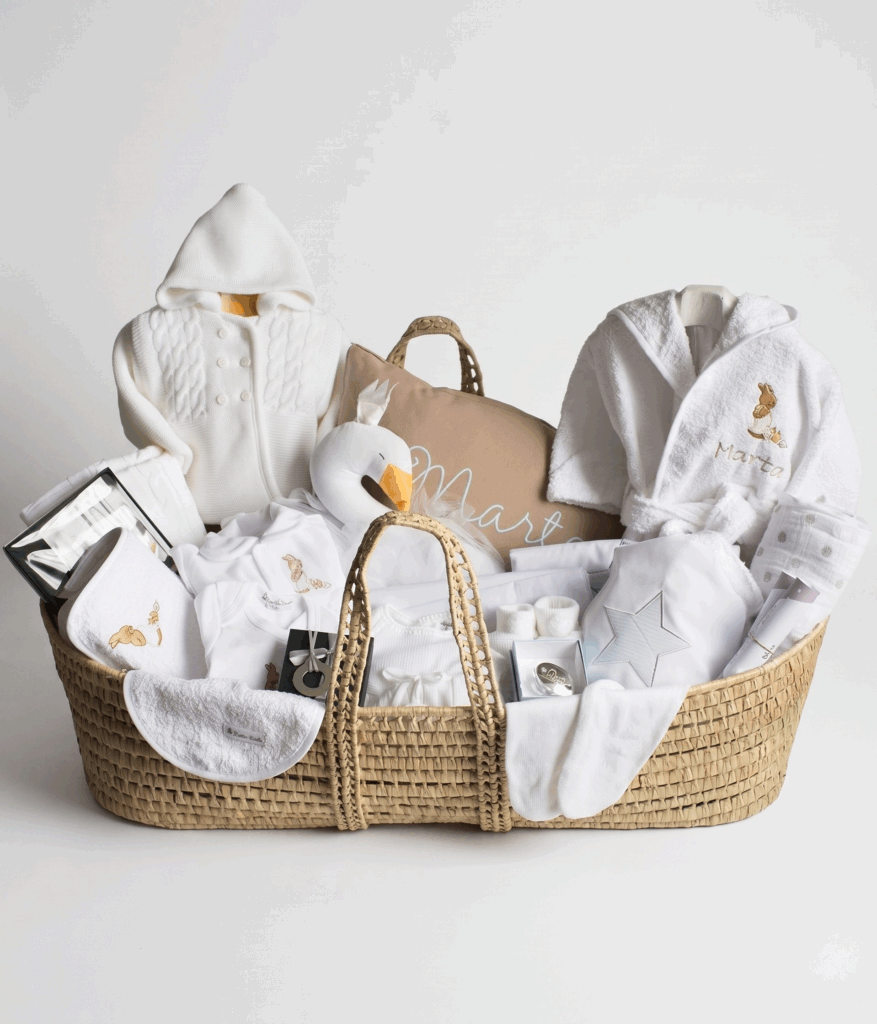 Gran canastilla de bebé en capazo de mimbre con chaqueta de punto, albornoz bordado, peluche de cisne y manta.