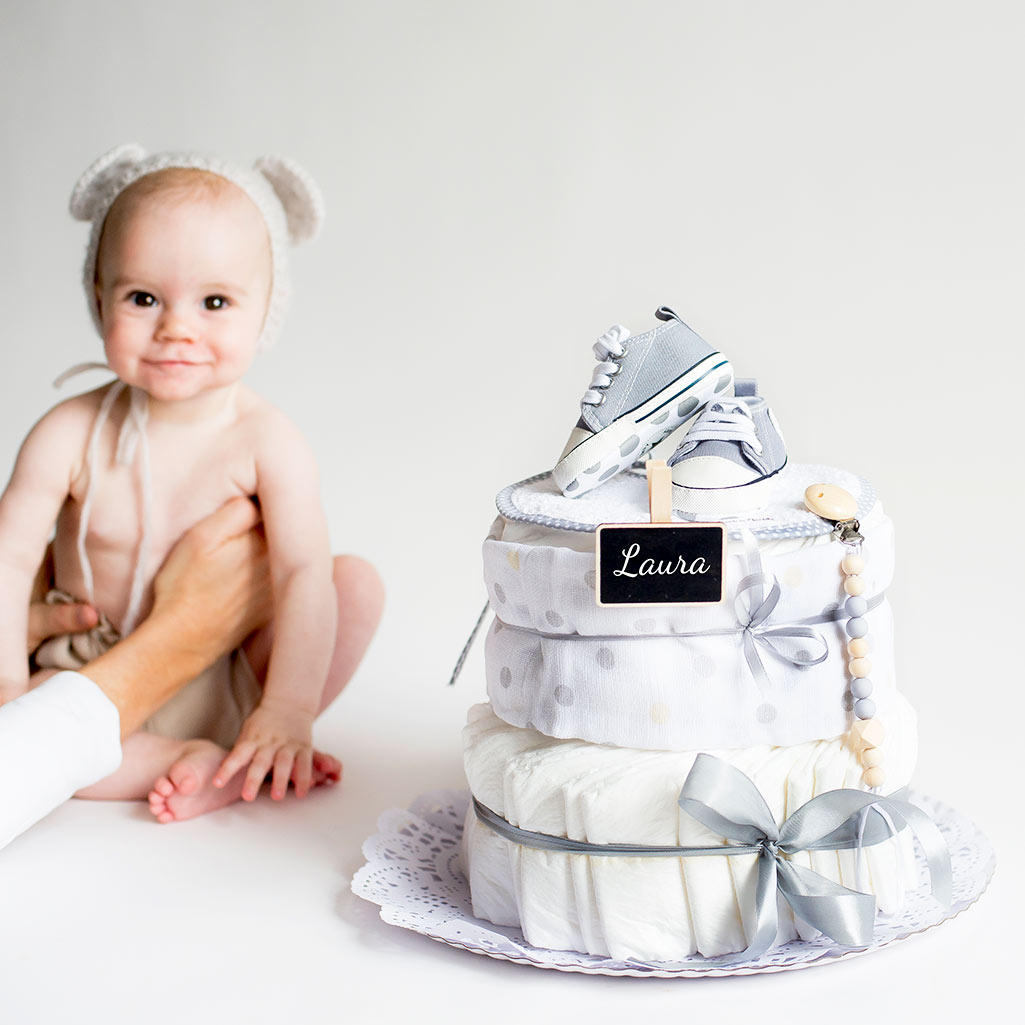 Tarta de pañales personalizada con nombre del bebé, zapatitos y accesorios infantiles.